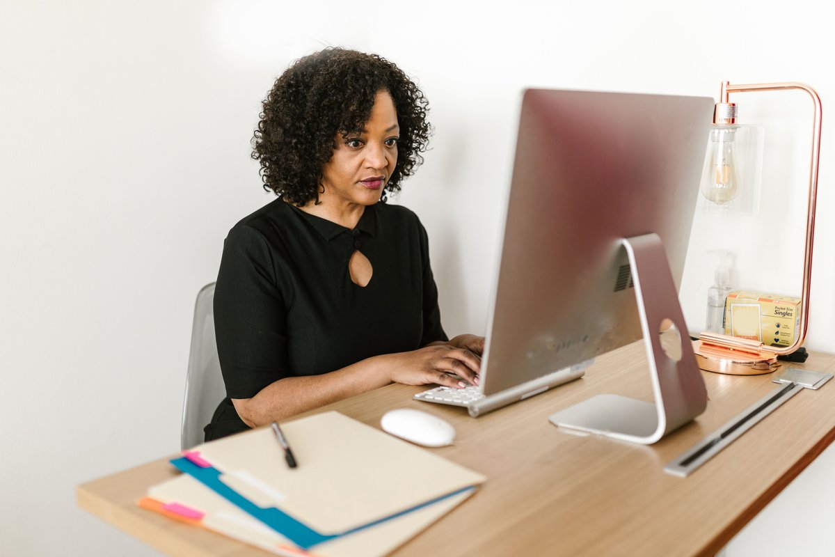A woman working on a desktop computer at a tidy office desk with a paper file folder.